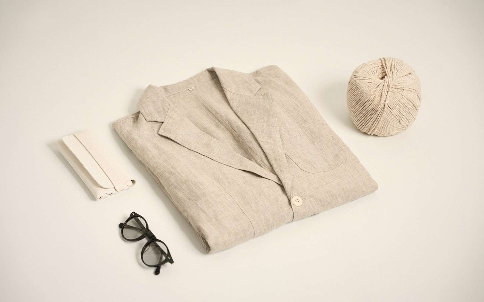 Folded linen blazer beside eyeglasses, a case, and a ball of yarn