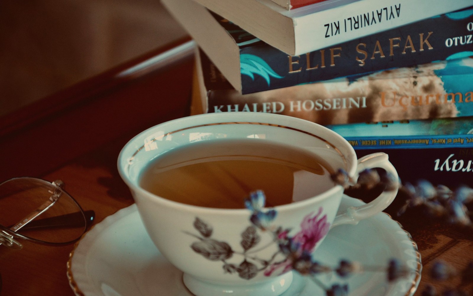 A floral teacup filled with tea sits beside a stack of books and glasses