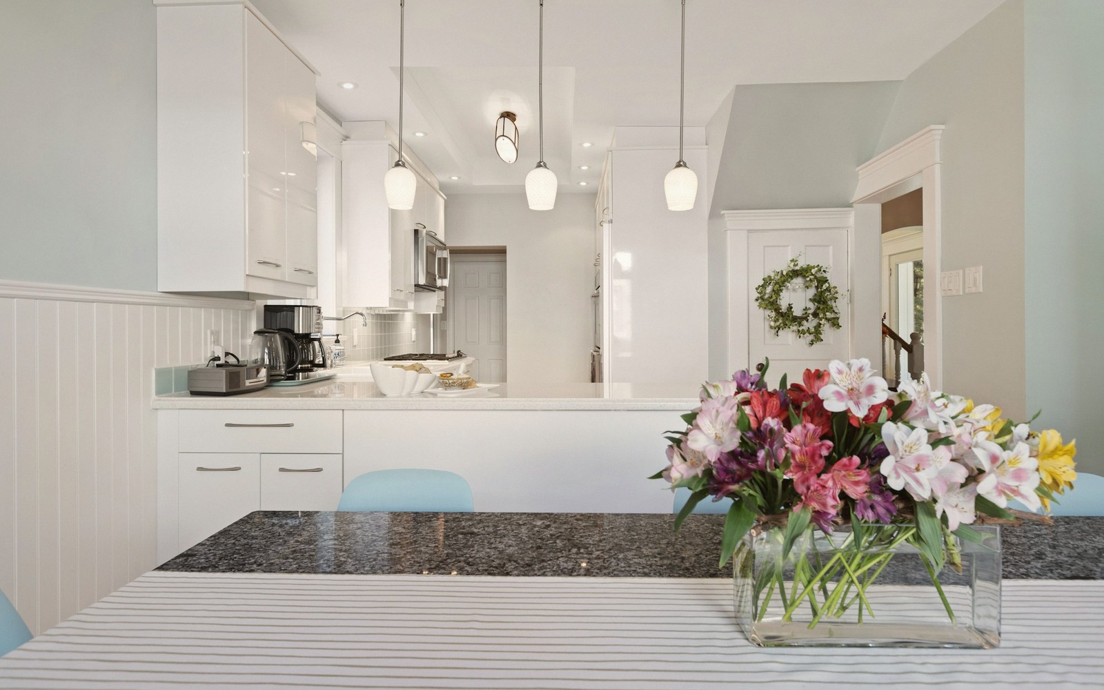 White kitchen with pendant lights and a vase of colorful flowers on the counter