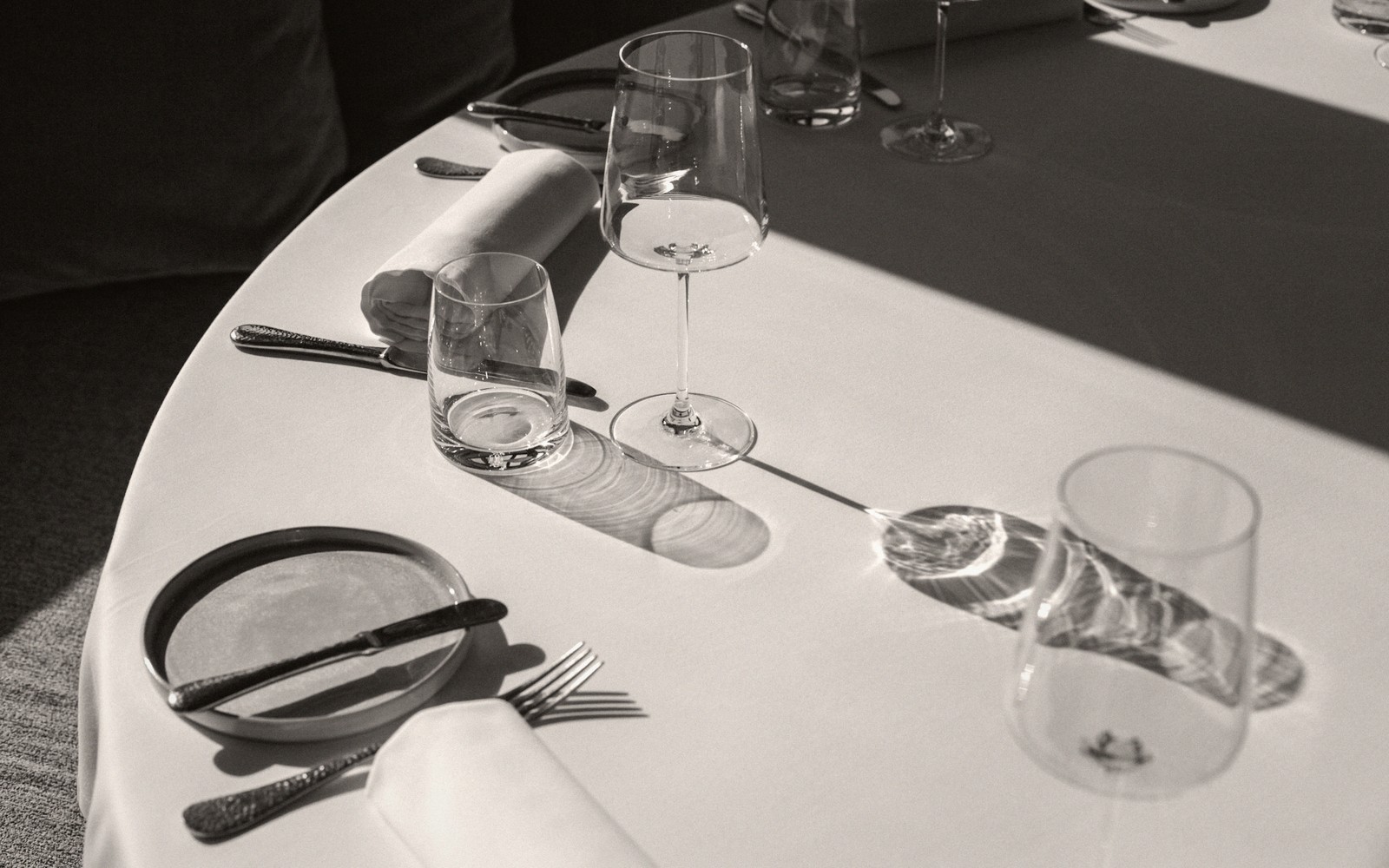 Sunlit table setting with wine glasses casting long shadows across a white cloth